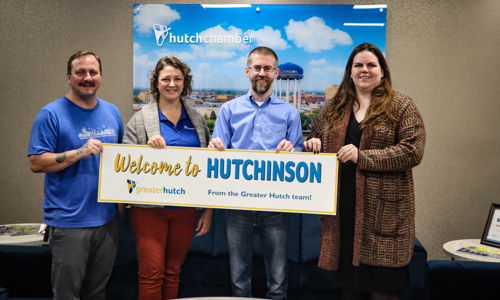 Four smiling people hold a "Welcome to HUTCHINSON" sign, creating a warm, inviting atmosphere in a community setting.