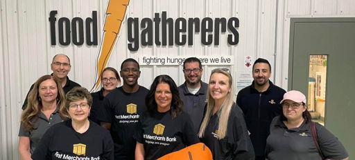 A joyful group in matching shirts poses with a large carrot prop, symbolizing community spirit and commitment to food assistance.