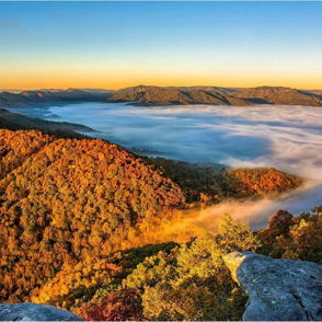 Rolling mountains in vibrant autumn foliage, illuminated by sunrise, evoke peace and tranquility amidst gentle fog.