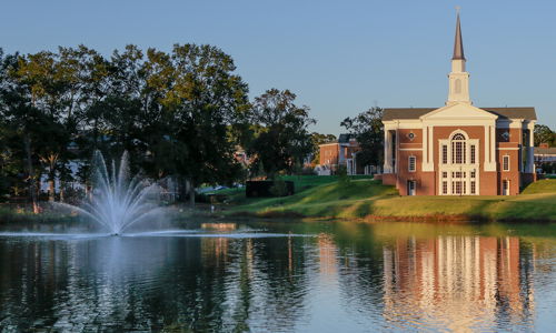A peaceful landscape with a church by a calm lake, surrounded by greenery and soft sunlight, evoking serenity and spirituality.