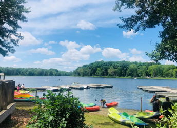 Scenic lakeside view with colorful kayaks, calm water, and lush trees, evoking joy, adventure, tranquility, and nature connection.
