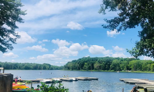 Scenic lakeside view with colorful kayaks, calm water, and lush trees, evoking joy, adventure, tranquility, and nature connection.