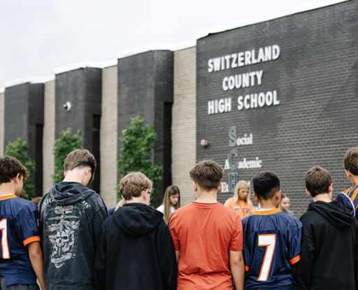 Students in jerseys stand united in front of a high school, exuding camaraderie and anticipation for a meaningful event.