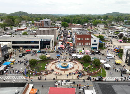 Bustling small-town scene with a fountain, shops, and vibrant festival atmosphere filled with joy and community.