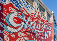 Vibrant mural on a brick wall, featuring "Glasgow" in bold colors, evoking creativity and community pride.