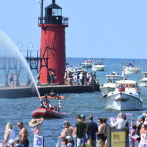 Vibrant summer waterfront scene with a red lighthouse, boats, people enjoying festivities, and a lively fountain spray.