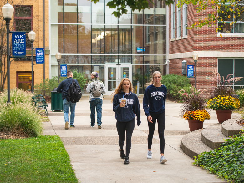 Campus scene with students walking, chatting in a vibrant, green setting, showcasing community and a lively atmosphere.