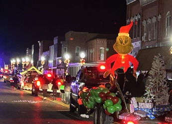 Festive nighttime parade scene with decorated vehicles, balloons, and a Grinch inflatable, evoking joy and community spirit.
