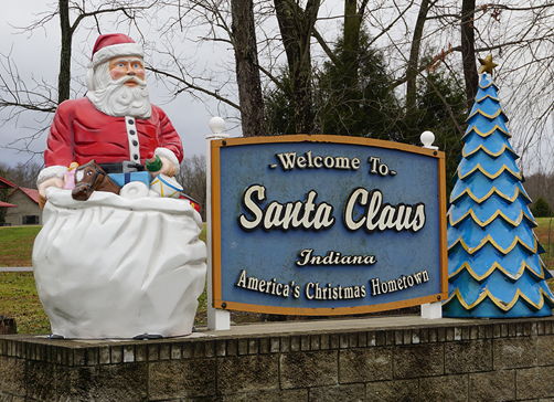 Whimsical welcome sign in Santa Claus, Indiana, featuring a Santa statue and festive Christmas tree, evoking holiday cheer.