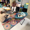 Three individuals engage collaboratively on a colorful rug in a cozy learning space, fostering warmth and inclusivity.