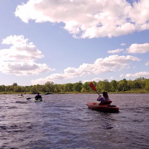 Kayakers paddle on a calm river under a bright sky with fluffy clouds, evoking tranquility and joy in nature.