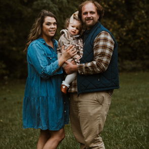 A joyful family stands outdoors in a grassy area, conveying warmth, love, and togetherness in a playful, relaxed atmosphere.