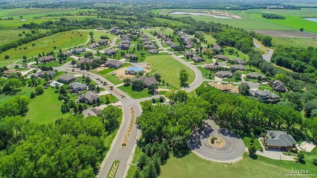 Aerial view of a serene suburban neighborhood surrounded by greenery, featuring winding roads, homes, and a central roundabout.