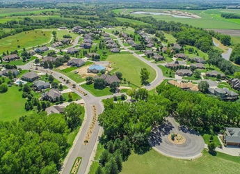 Aerial view of a serene suburban neighborhood surrounded by greenery, featuring winding roads, homes, and a central roundabout.