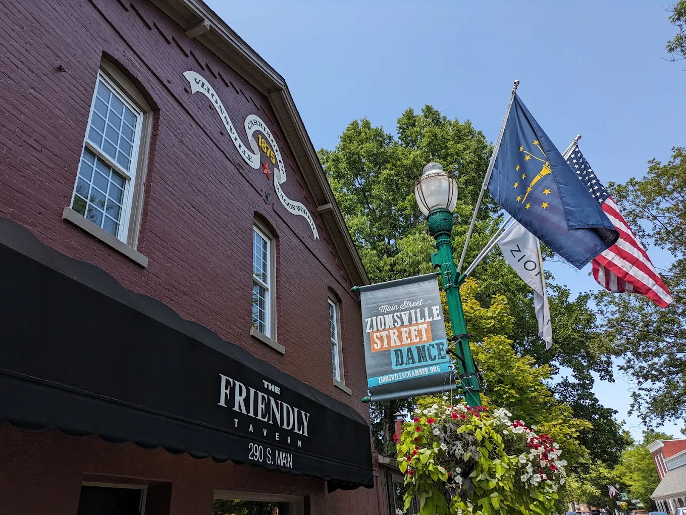 Charming maroon building with "FRIENDLY" awning, murals, flags, and greenery, creating a vibrant atmosphere for local events.