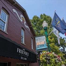 Charming maroon building with "FRIENDLY" awning, murals, flags, and greenery, creating a vibrant atmosphere for local events.