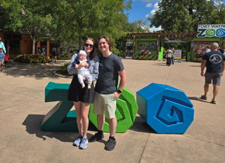 Family joyfully poses by colorful "ZOO" letters on a sunny day, showcasing warmth and togetherness during their outing.