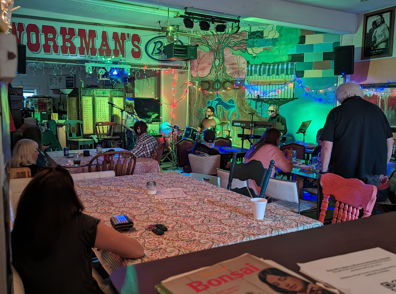 Lively interior of "Workman's" bar, vibrant lighting, patrons socializing, evoking relaxation and enjoyment in a festive atmosphere.