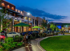 Vibrant urban outdoor space at night with cozy seating, greenery, lights, and people enjoying a lively, inviting atmosphere.