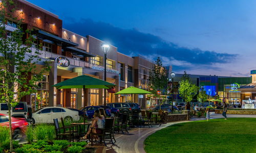 Vibrant urban outdoor space at night with cozy seating, greenery, lights, and people enjoying a lively, inviting atmosphere.