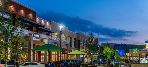 Vibrant urban outdoor space at night with cozy seating, greenery, lights, and people enjoying a lively, inviting atmosphere.