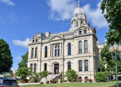 Elegant historical building with clock tower, surrounded by lawns and trees, under a clear blue sky, evoking civic pride and warmth.