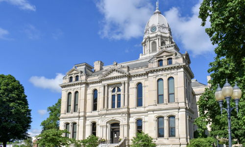 Elegant historical building with clock tower, surrounded by lawns and trees, under a clear blue sky, evoking civic pride and warmth.