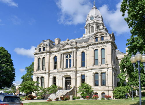 Elegant historical building with clock tower, surrounded by lawns and trees, under a clear blue sky, evoking civic pride and warmth.