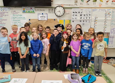 A joyful group of children in colorful outfits pose together in a classroom, celebrating a special occasion with smiles.