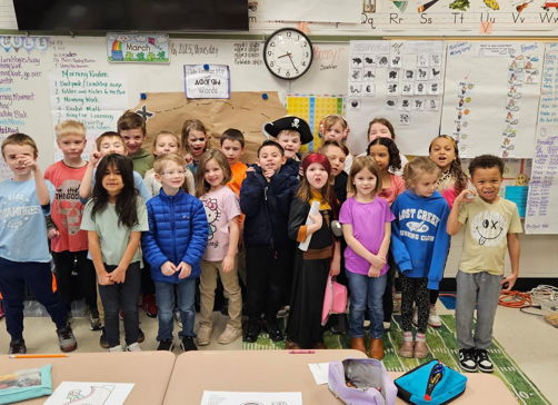 A joyful group of children in colorful outfits pose together in a classroom, celebrating a special occasion with smiles.