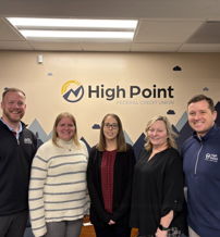 Five smiling professionals in an office with High Point Federal Credit Union logo suggest unity, confidence, and a welcoming atmosphere.