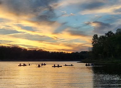 Tranquil sunset over a lake with warm hues, reflecting boats/kayakers, evoking peace and connection with nature.