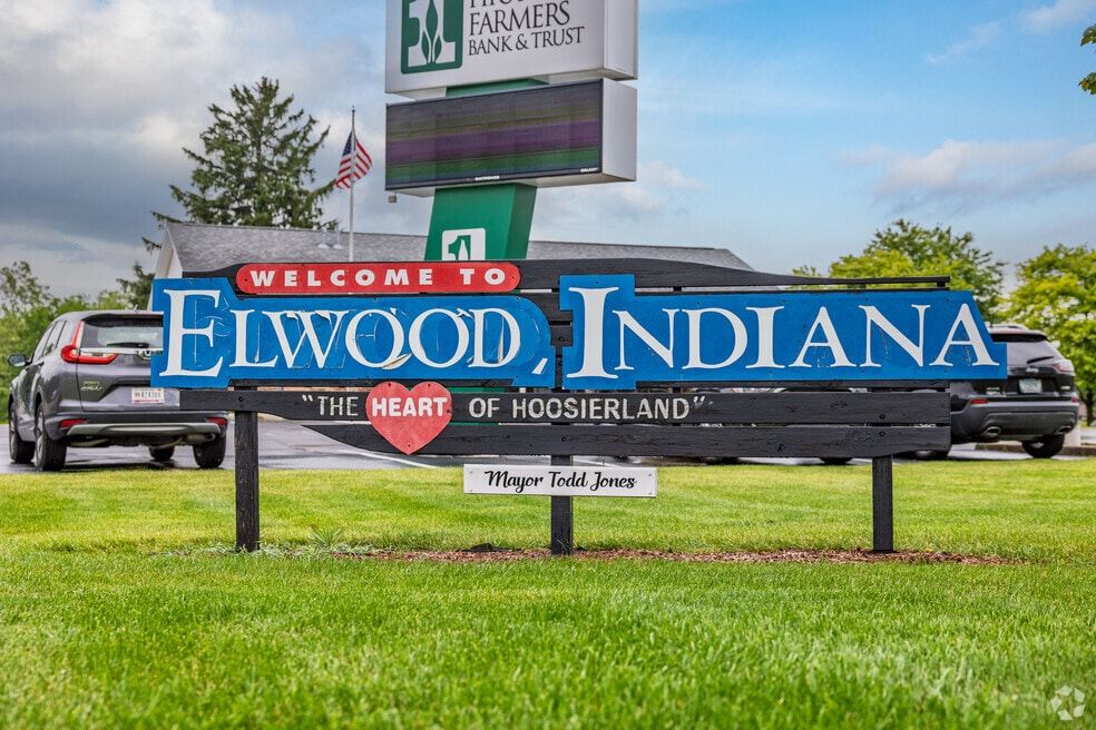 Welcoming sign for Elwood, Indiana, bright colors, "THE HEART OF HOOSIERLAND," with greenery and clear skies.