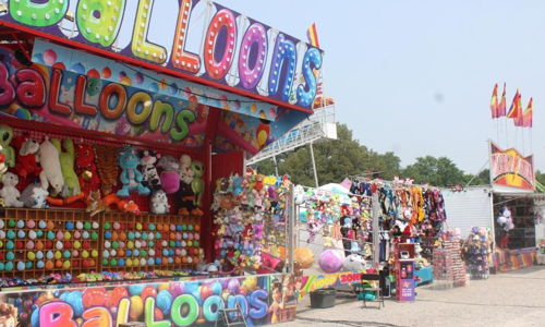 A vibrant carnival scene with colorful balloon and plush toy stalls, evoking nostalgia and joyful excitement.