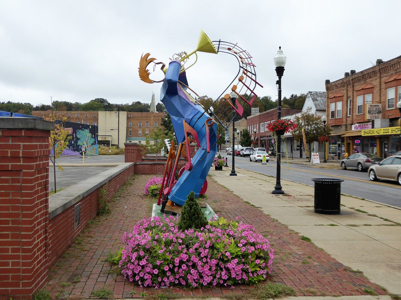 Vibrant sculpture of a trumpeter in urban setting, surrounded by flowers, radiating joy and artistic expression.