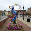 Vibrant sculpture of a trumpeter in urban setting, surrounded by flowers, radiating joy and artistic expression.
