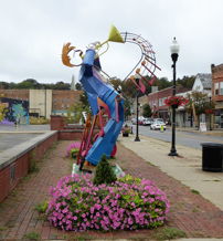Vibrant sculpture of a trumpeter in urban setting, surrounded by flowers, radiating joy and artistic expression.