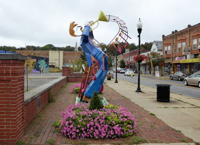 Vibrant sculpture of a trumpeter in urban setting, surrounded by flowers, radiating joy and artistic expression.