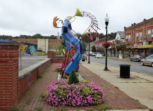 Vibrant sculpture of a trumpeter in urban setting, surrounded by flowers, radiating joy and artistic expression.