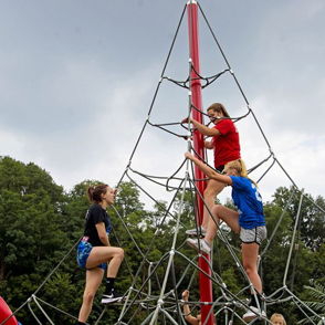 Children climb a tall red climbing structure at a playground, showcasing adventure and teamwork under an overcast sky.