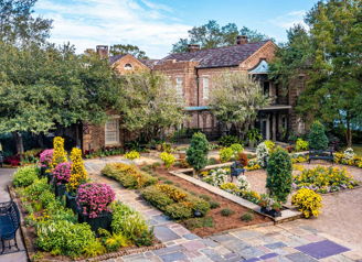 Charming brick house amid lush greenery and vibrant flower garden, evoking peace, joy, and harmony with nature.