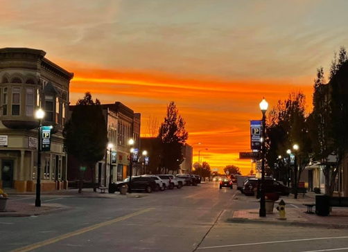 Sunset street scene with vibrant colors, charming buildings, warm streetlights, evoking calmness, nostalgia, hopefulness, and affection.