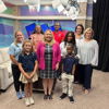 A joyful group photo in a studio, showcasing community, warmth, and confidence among smiling adults and children.