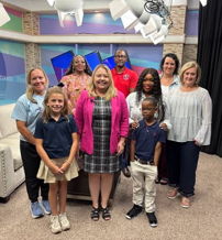A joyful group photo in a studio, showcasing community, warmth, and confidence among smiling adults and children.