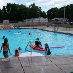 A lively pool scene with children and adults enjoying summer fun, swimming, playing, and sliding, filled with joy and laughter.