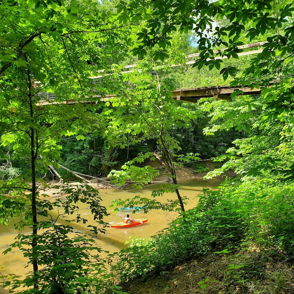 A serene scene with a kayak on calm water, surrounded by lush greenery and a bridge in the background, evoking tranquility.