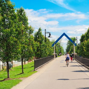 Pathway lined with trees under a clear sky, leading to an archway; a person walks, evoking tranquility and hope.