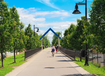 Pathway lined with trees under a clear sky, leading to an archway; a person walks, evoking tranquility and hope.
