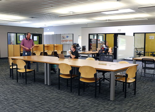 Modern open workspace with tables, laptops, and people collaborating, creating a community-focused, productive atmosphere.