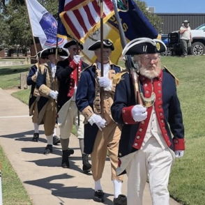 Historical military uniformed individuals participate in a patriotic procession, showcasing flags and evoking pride and unity.